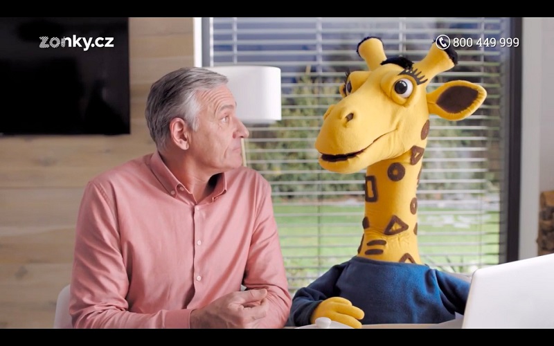 V reklamě mu sekunduje maskot v podobě žirafy. 